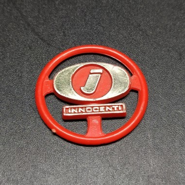 Fregio Innocenti in plastica rossa con dettagli dorati. Segni sul retro