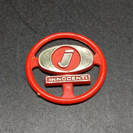 Fregio Innocenti in plastica rossa con dettagli dorati. Segni sul retro